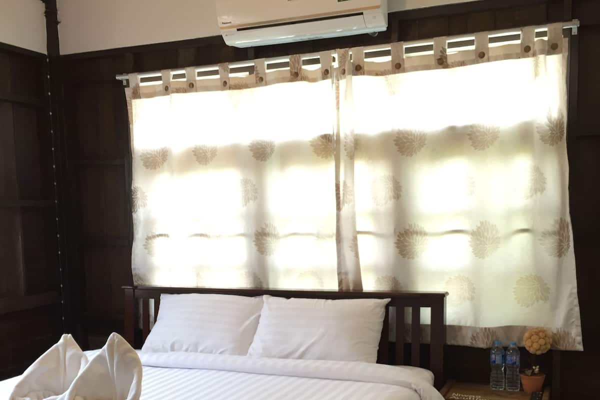 A neatly made bed with white linens, a wooden headboard, and a small bedside table with a remote control, water bottles, and a potted plant.