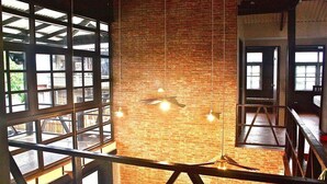 A high-ceilinged room with exposed brick walls, large windows, and a hanging light fixture.