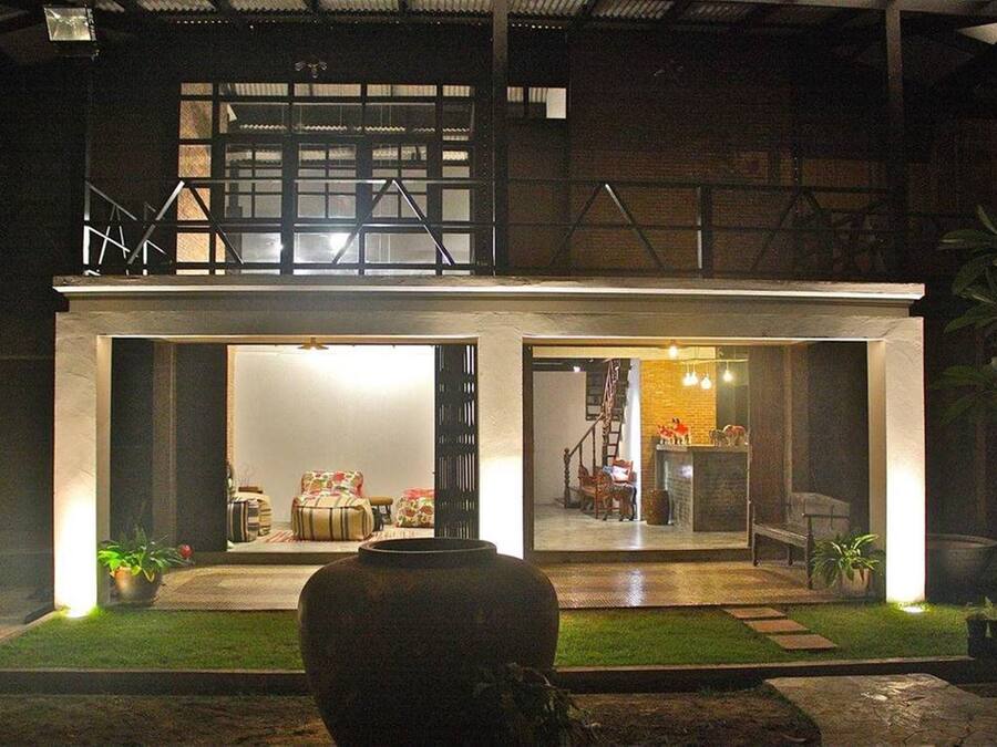 Um edifício moderno com duas entradas abertas, um vaso grande em primeiro plano e uma escadaria que leva a um segundo andar.