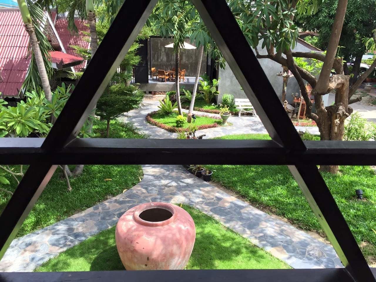 A garden with a stone pathway, a large pink pot, and a seating area with chairs and a table.