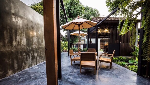An outdoor seating area with wooden chairs and tables, surrounded by greenery and a concrete floor.