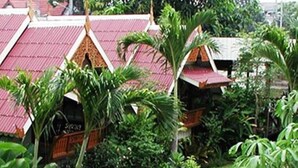 A courtyard with a stone pathway, lush greenery, and traditional buildings with red roofs.