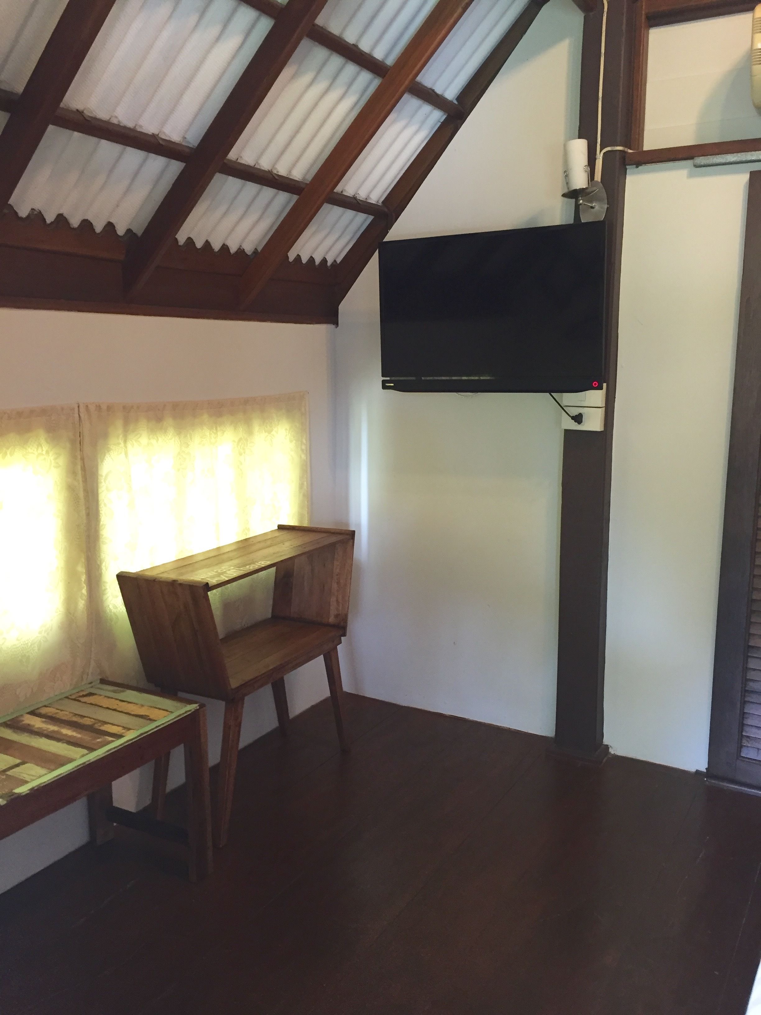 Una habitación con un escritorio de madera, un televisor en la pared y una ventana con cortinas.