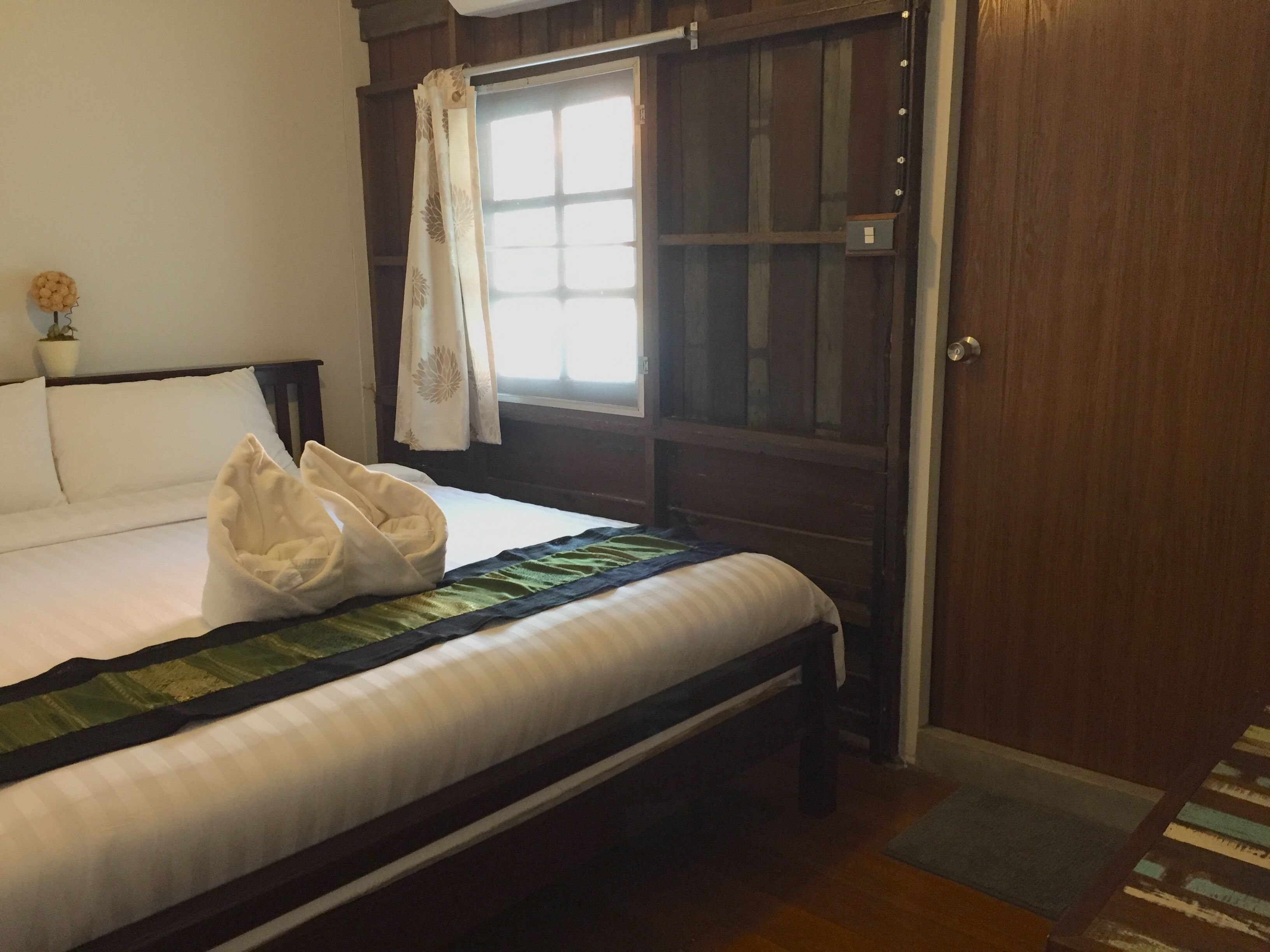 Un dormitorio con cama, una ventana con cortinas, una puerta de madera y una pequeña planta en maceta.