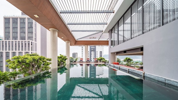 Une piscine intérieure moderne, dotée d’une eau cristalline, entourée de verdure et de grandes fenêtres offrant une vue sur la ville.