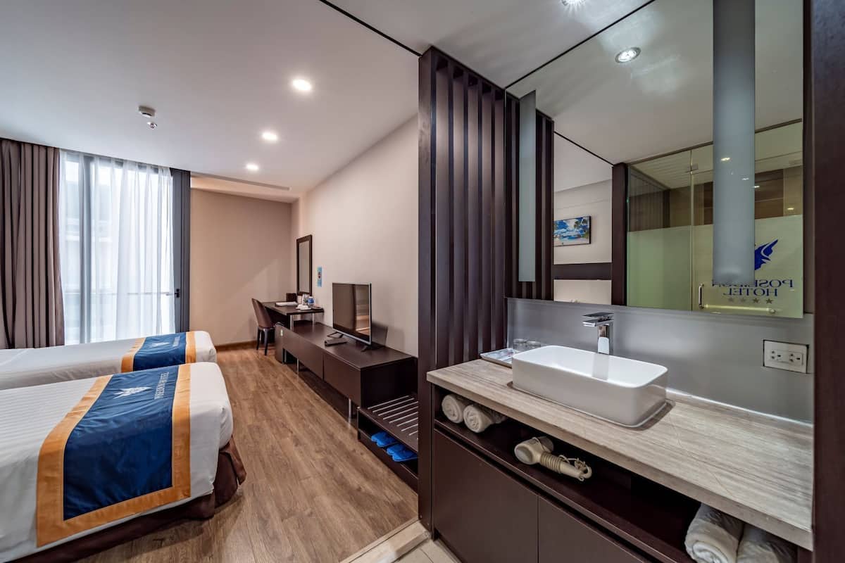 Een hotelkamer met twee bedden, een bureau met televisie, een grote spiegel en een badkamer met wastafel en douche.