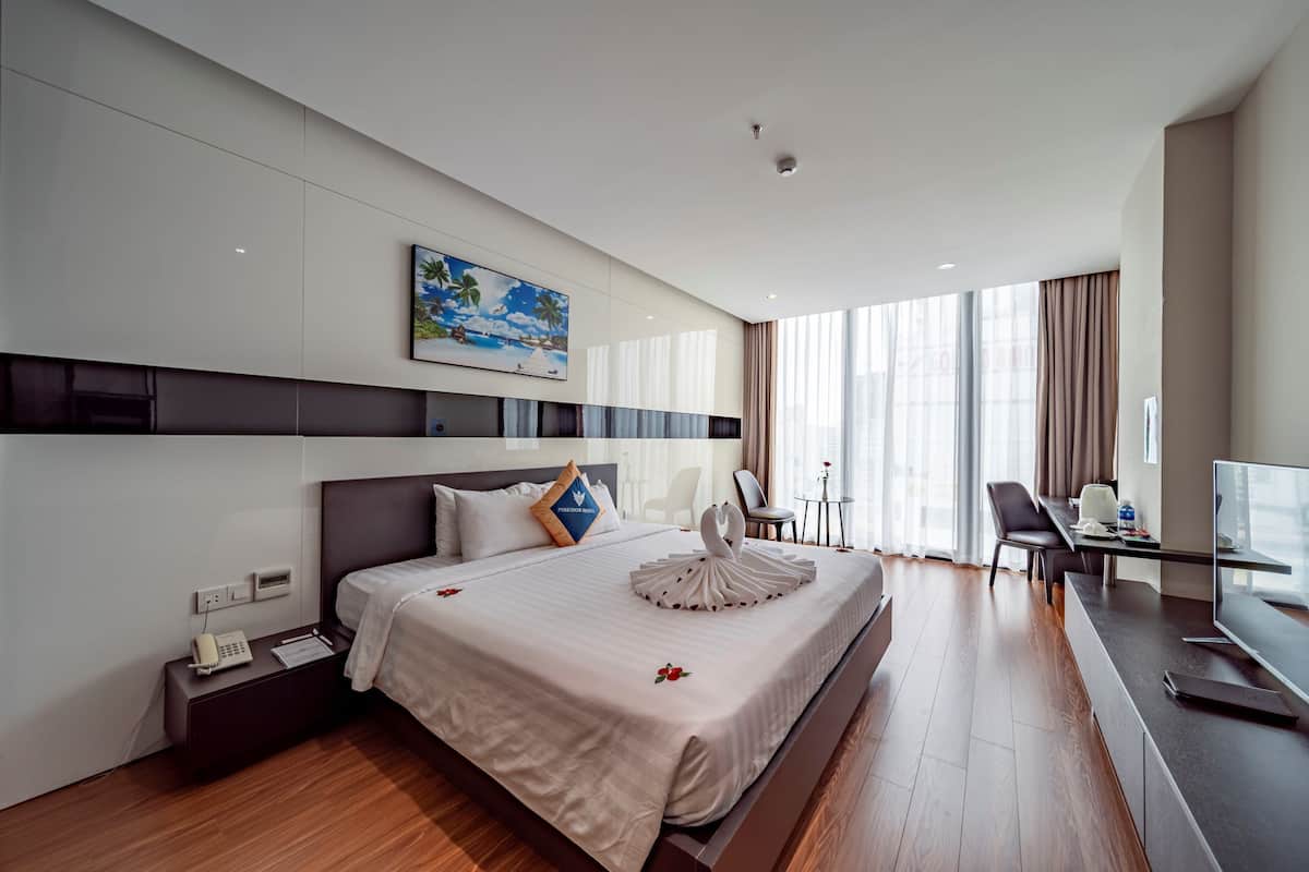 Een moderne hotelkamer met een groot bed, een bureau, een stoel, een televisie en een schilderij aan de muur.