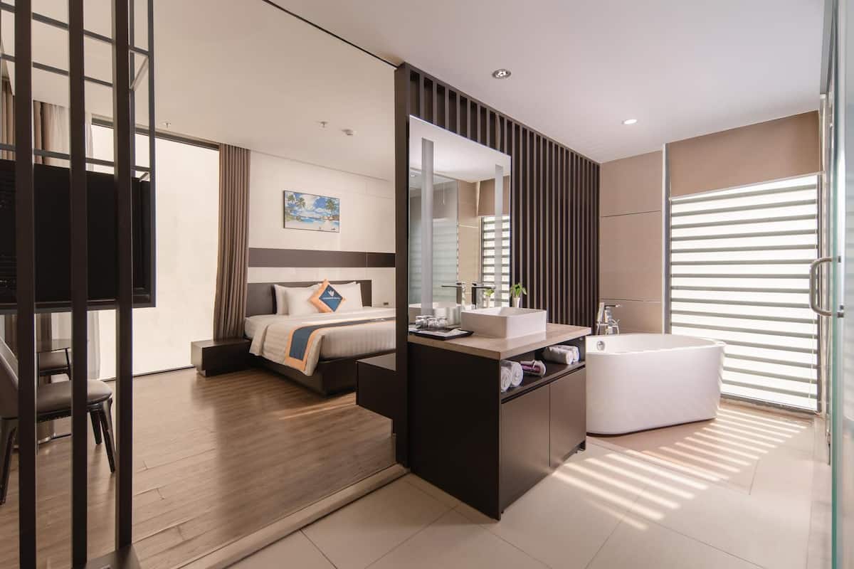 Een moderne hotelkamer met een bed, nachtkastje, spiegel en een groot bad.