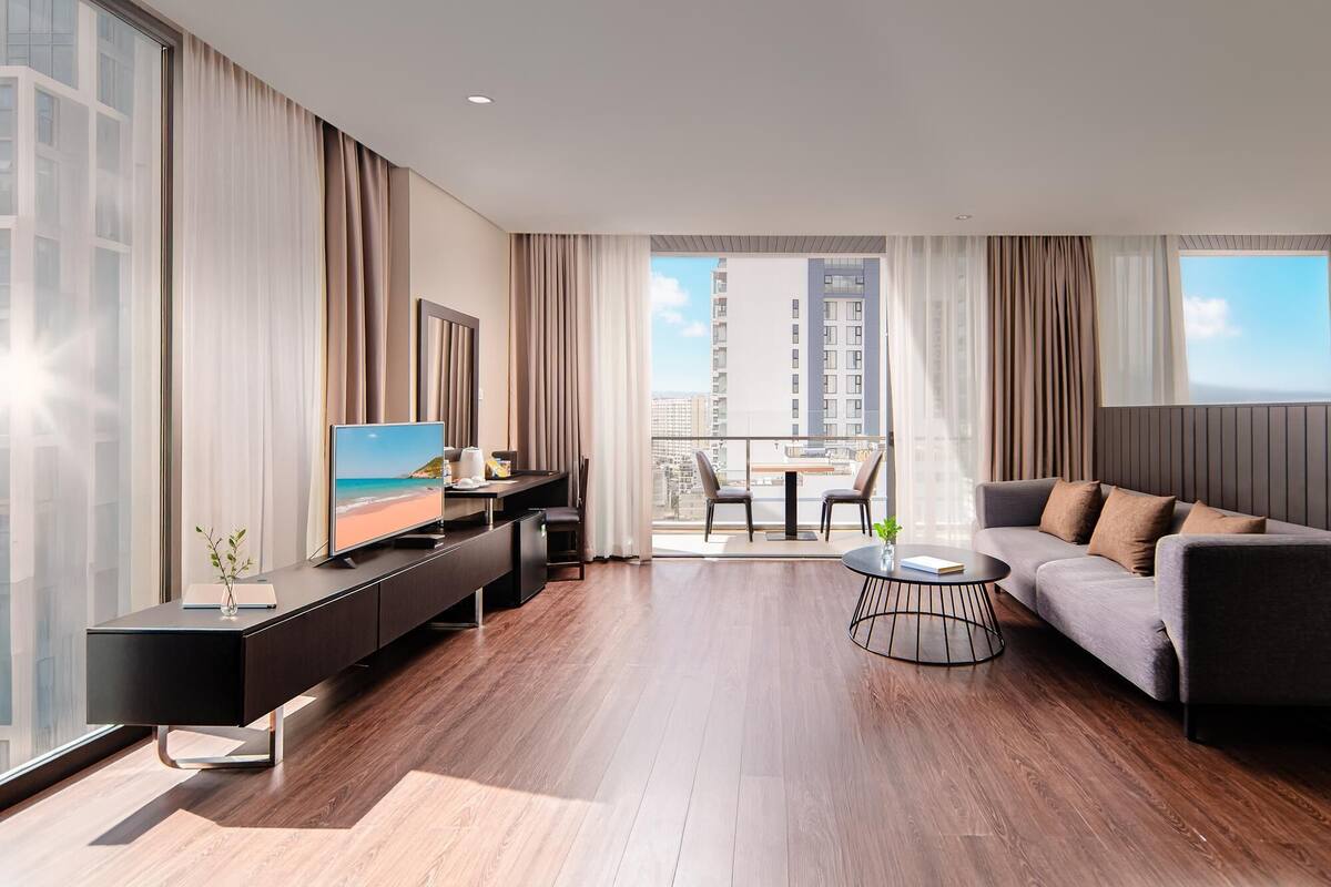 Een moderne woonkamer met een grote televisie, een bank, een eettafel en een balkon met uitzicht op de stad.