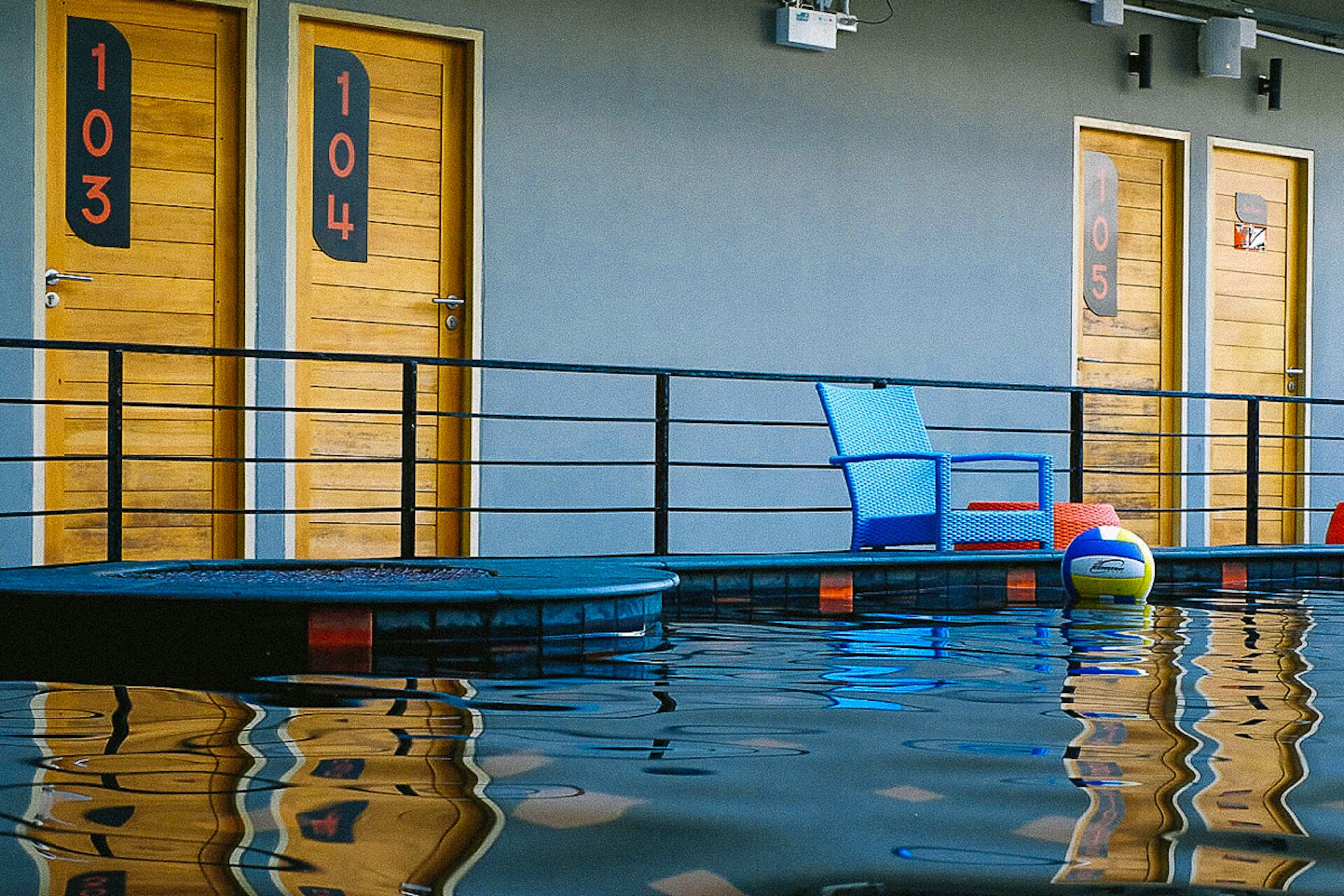 A pool area with a blue chair and a volleyball, surrounded by doors labeled 103, 104, and 105.