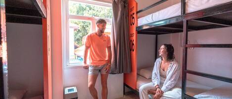 Un dormitorio con literas, una ventana con cortinas y un bote de basura.