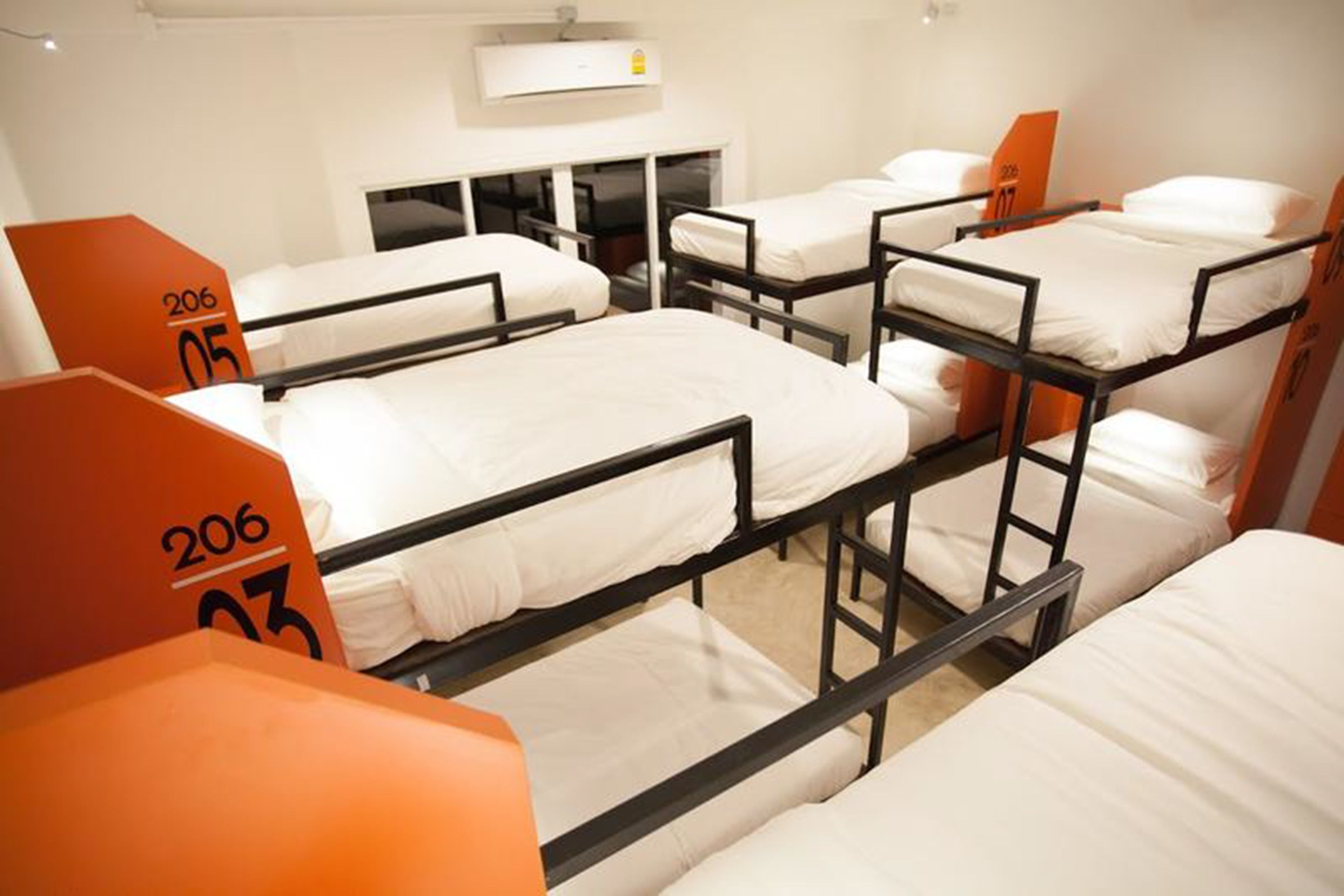A dormitory-style room with bunk beds, numbered room signs, and a white wall-mounted air conditioning unit.