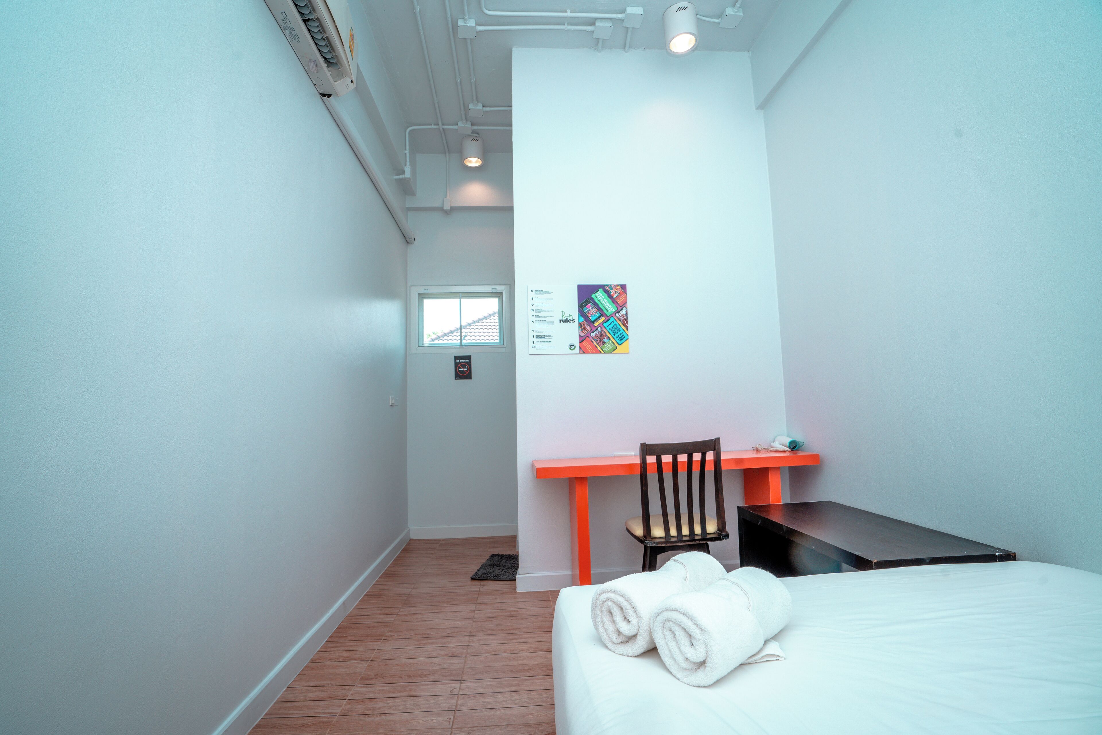 Habitación de hotel con cama, escritorio y silla. Se ve una ventana y una puerta.