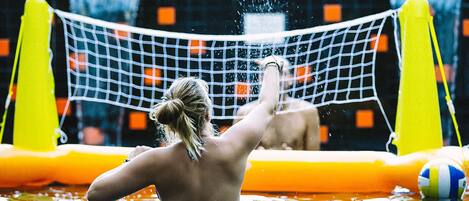 Eine Person spielt Volleyball im Pool mit aufblasbaren Absperrungen.