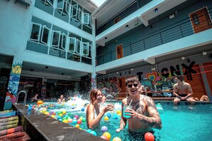 Piscina interior com vários níveis, bolas coloridas, área de bar e um muro com grafites.