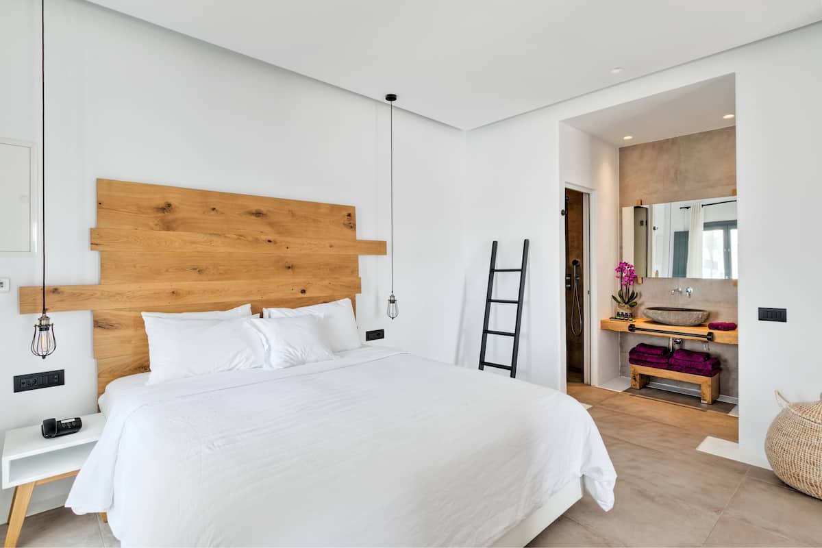 Een moderne slaapkamer met een houten hoofdeinde, een nachtkastje met een lamp, en een badkamer met een grote spiegel en wastafel.