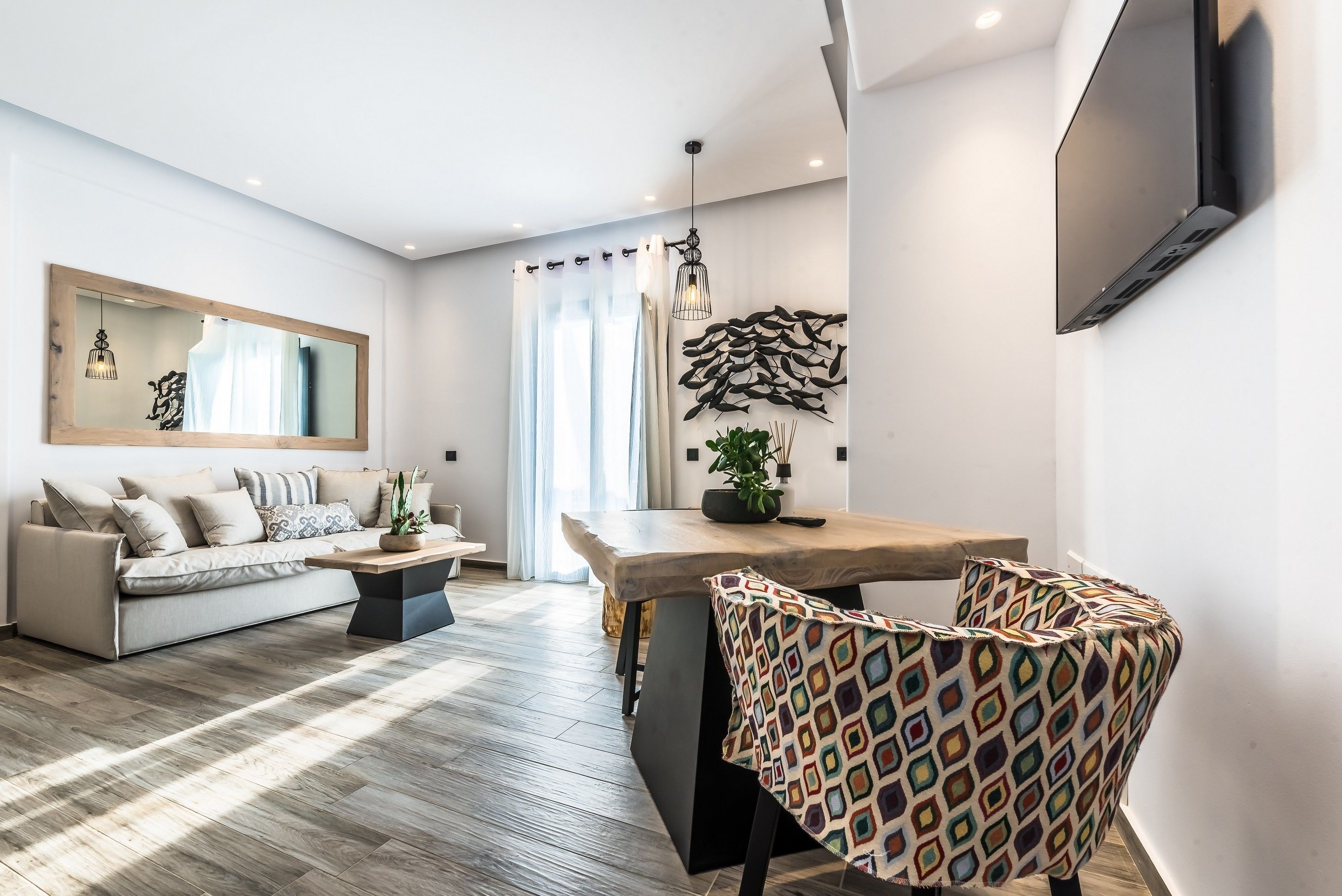 Una sala de estar moderna con un sofá, una mesa de centro, un sillón estampado, una mesa de comedor y un televisor montado en la pared.
