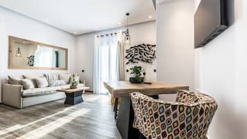 Una sala de estar moderna con un sofá, una mesa de centro, un sillón estampado, una mesa de comedor y un televisor montado en la pared.