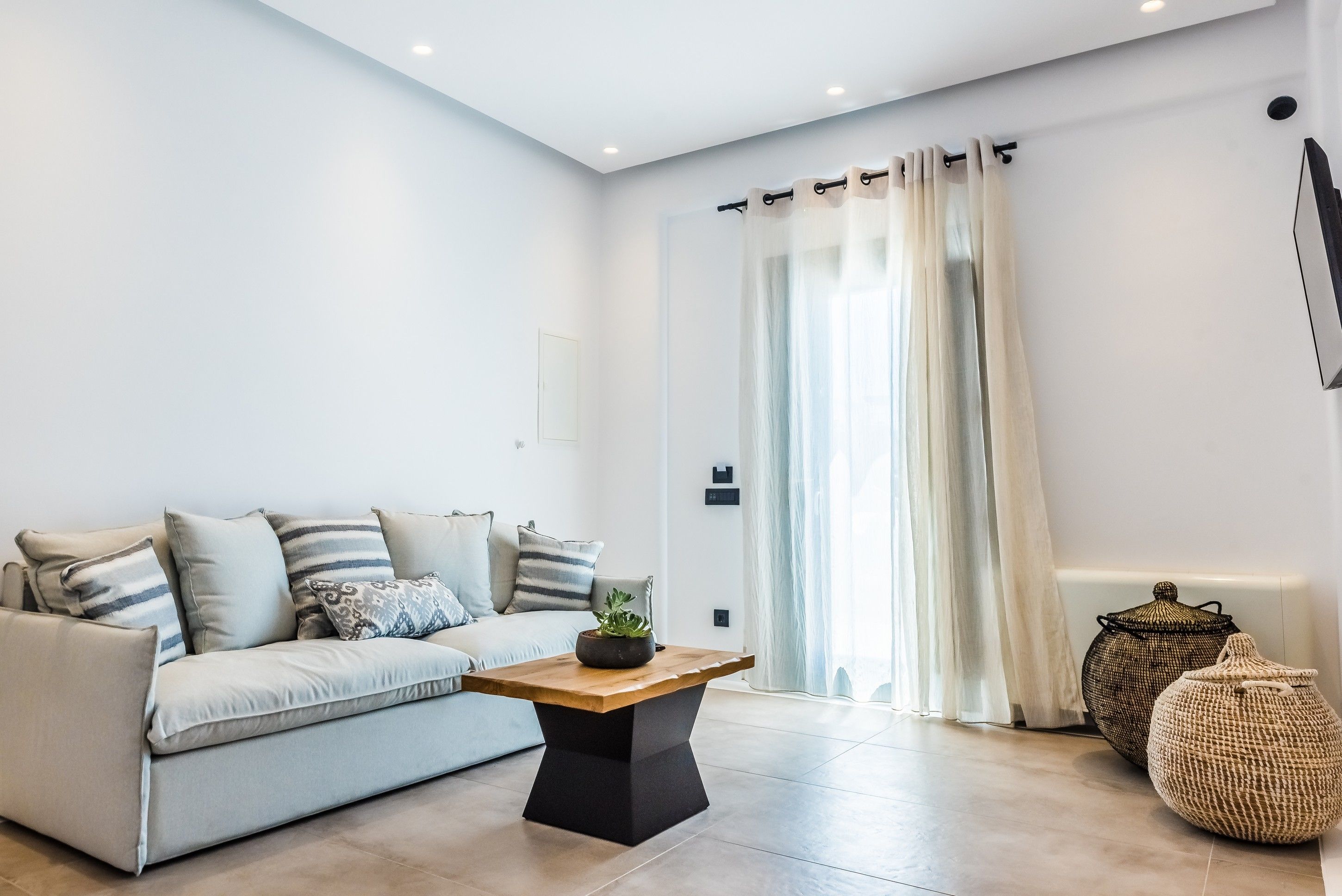 Ein modernes Wohnzimmer mit einem hellen Sofa, einem Holztisch und zwei gewebten Poufs.