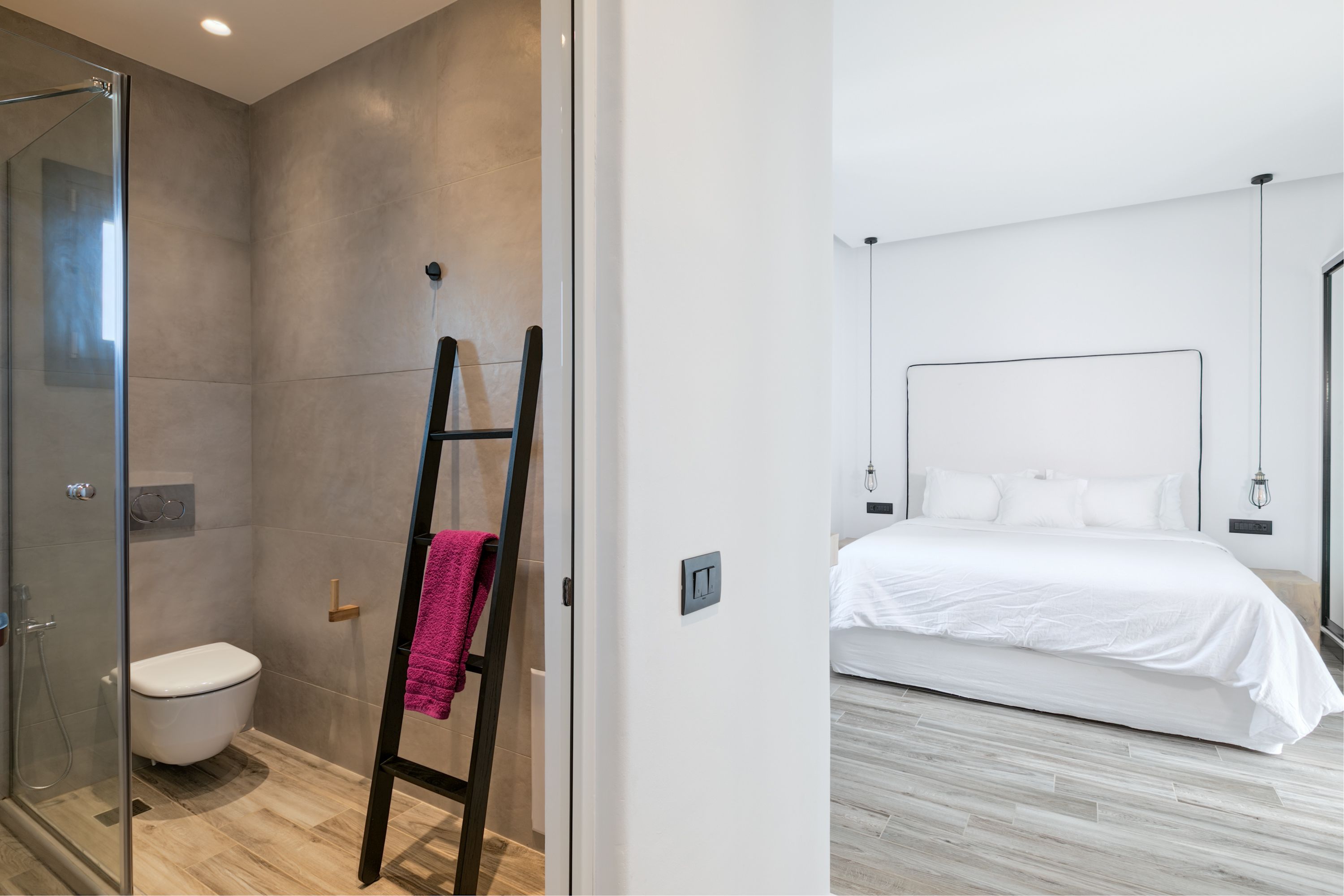 A modern bathroom with a glass shower enclosure, a white toilet, and a wooden ladder.
