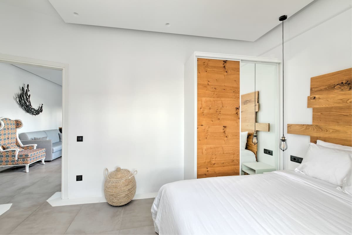 Een moderne slaapkamer met een groot bed, een houten hoofdbord, een geweven mand en een gestreept fauteuil.