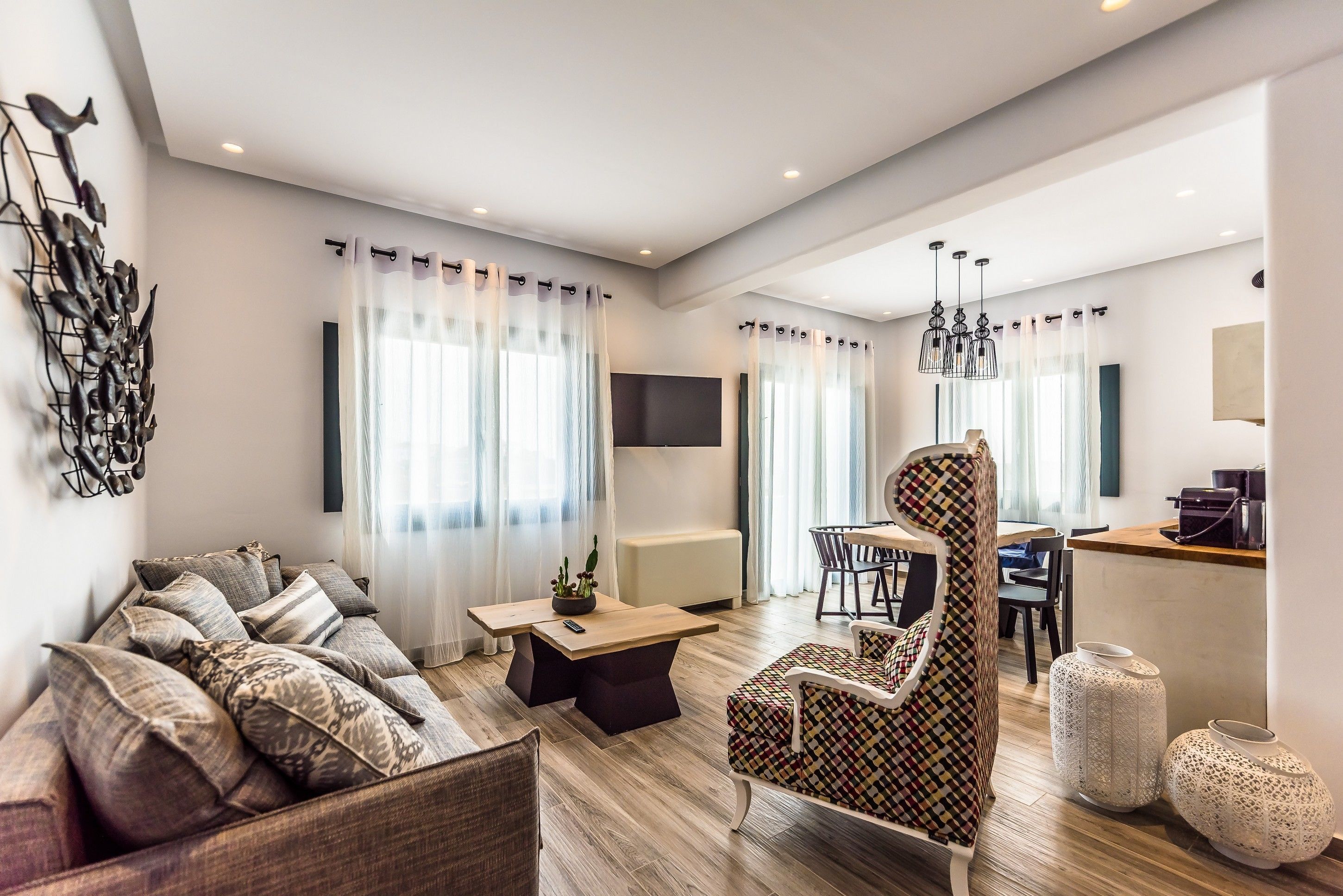 A modern living room with a sofa, a patterned armchair, a coffee table, and a dining area with chairs and a table.