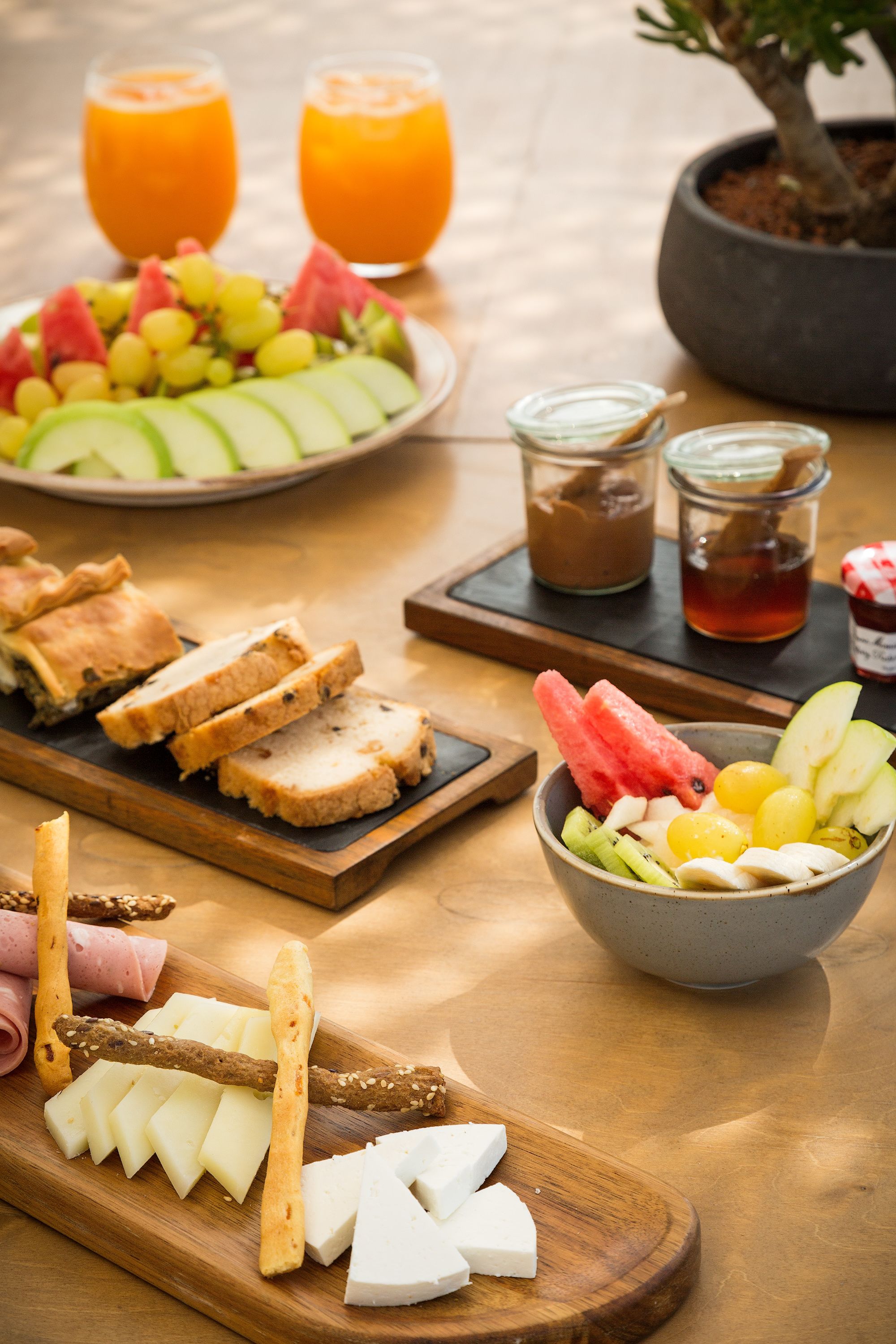 A table with various food items including sliced bread, cheese, fruits, and beverages.