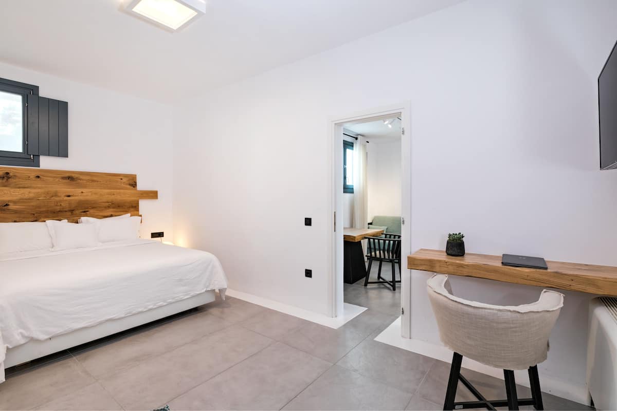 Een slaapkamer met een houten hoofdbord, een wit bed, een bureau met stoel en een kleine plant.