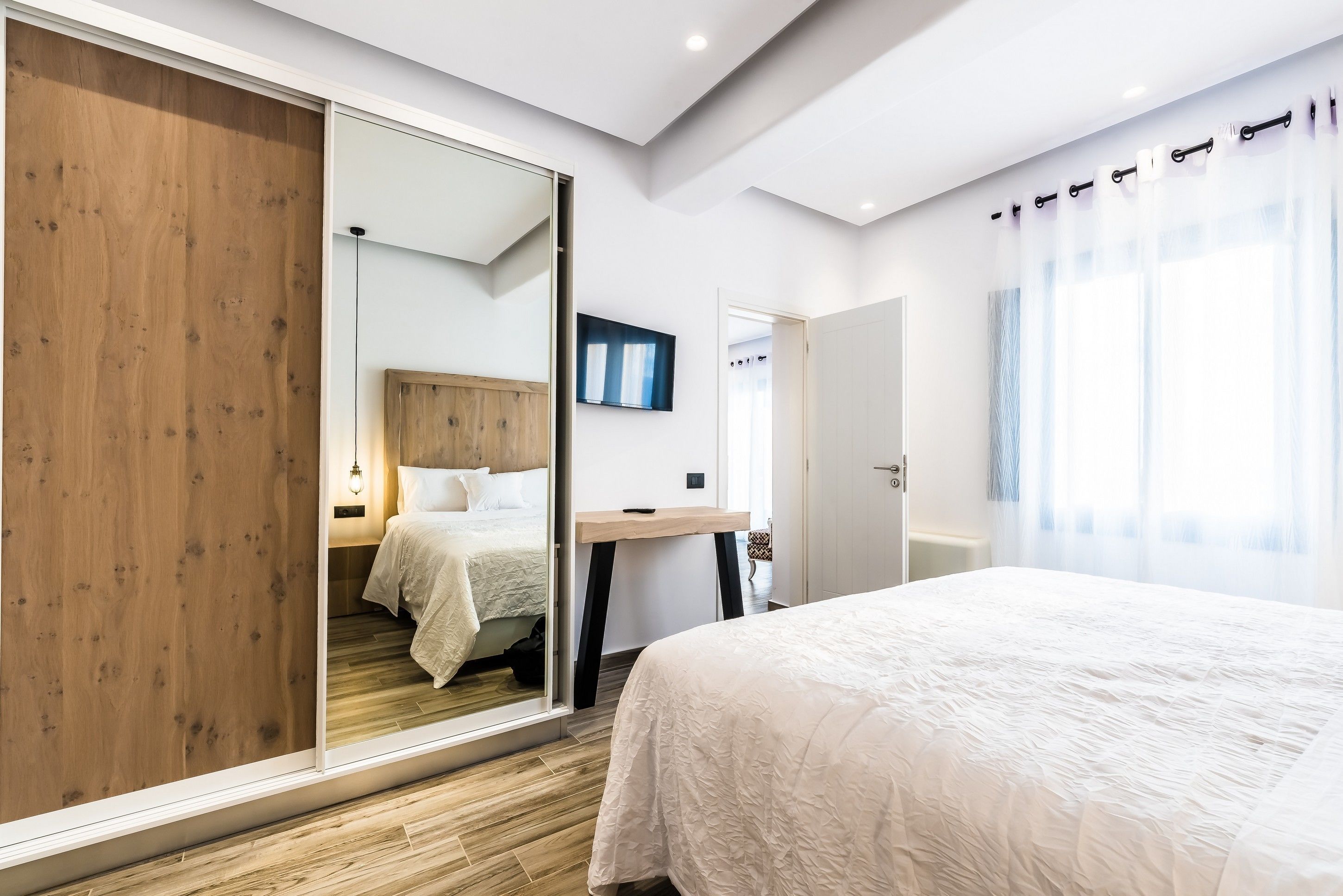 Een moderne slaapkamer met een groot bed, een houten garderobe, een bureau en een spiegel.