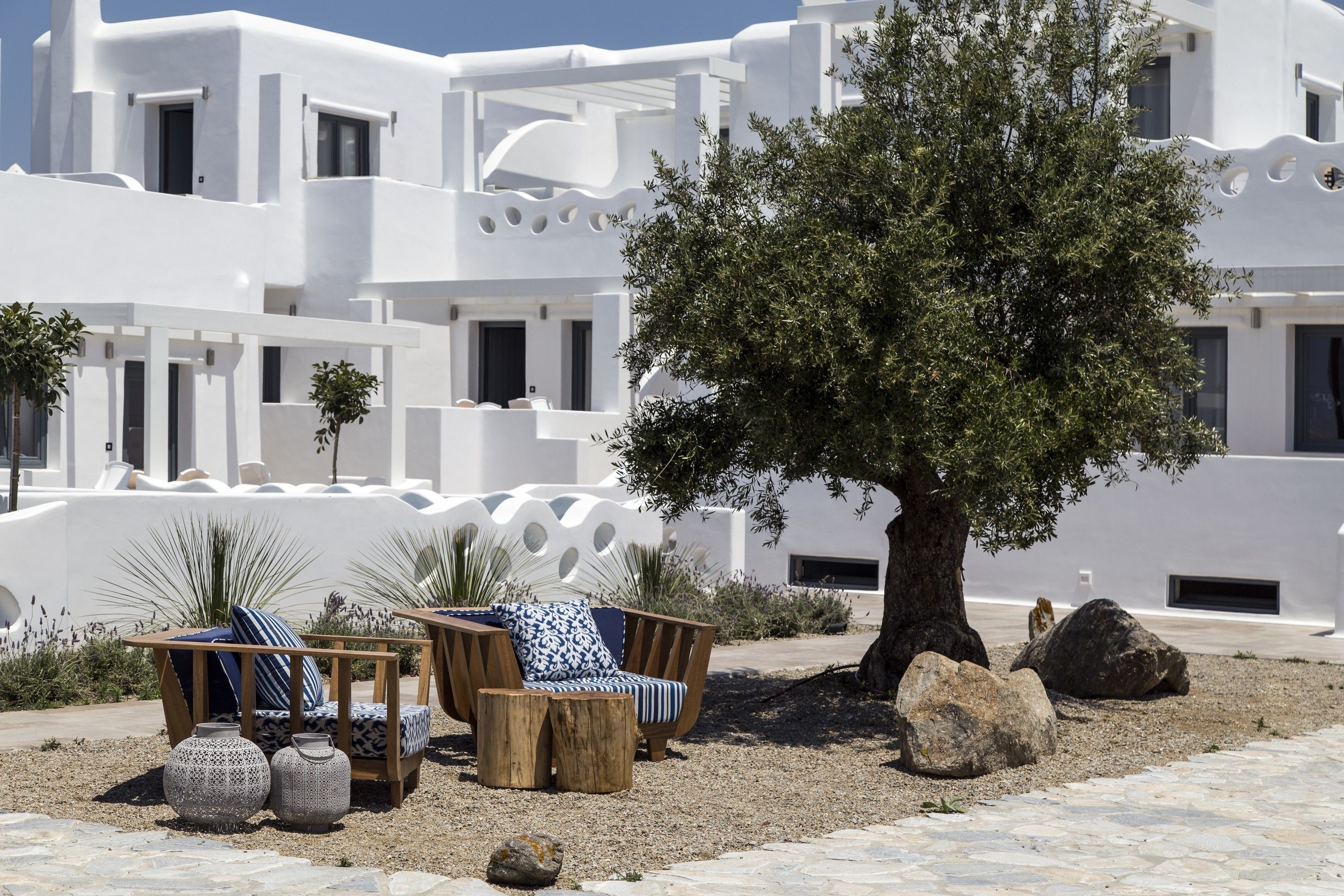 Edifici blanc amb un gran arbre al davant, zones d'seients exteriors amb coixins i gerros decoratius.
