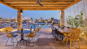 An outdoor patio with a pergola, seating, and a view of the cityscape. - Portes Mykonos Suites & Villas (Mykonos)