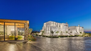 A modern building with large windows and a well-lit interior, featuring a dining area with a green chair and a table. - Portes Mykonos Suites & Villas (Mykonos)