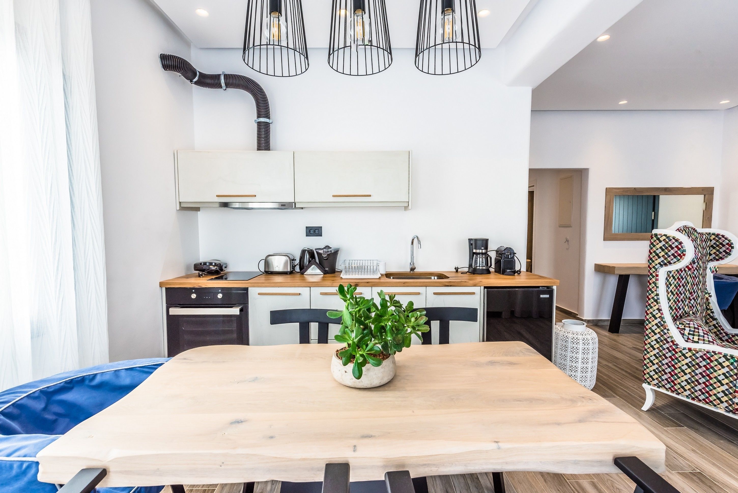 A modern kitchen with white cabinets, a wooden countertop, and a potted plant on the table.