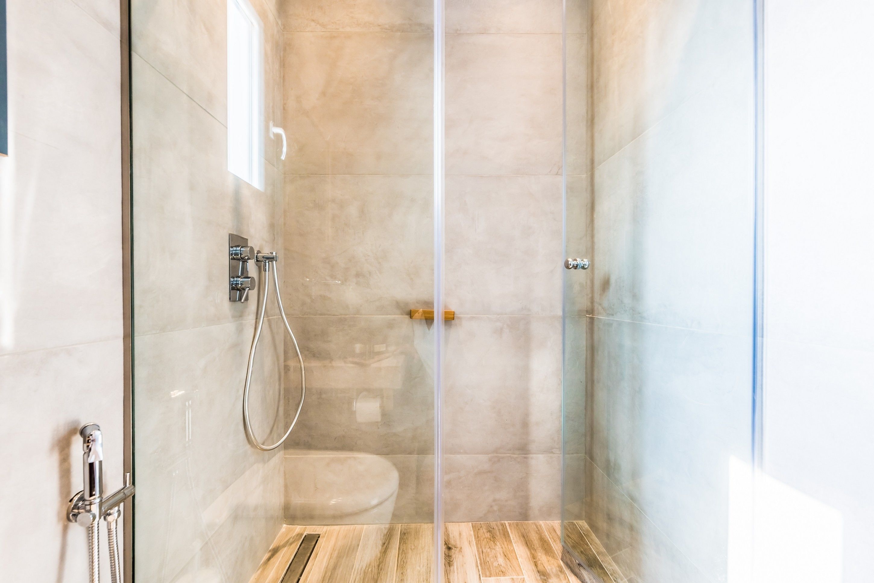 A glass-enclosed shower with a wooden floor and a toilet visible through the glass.