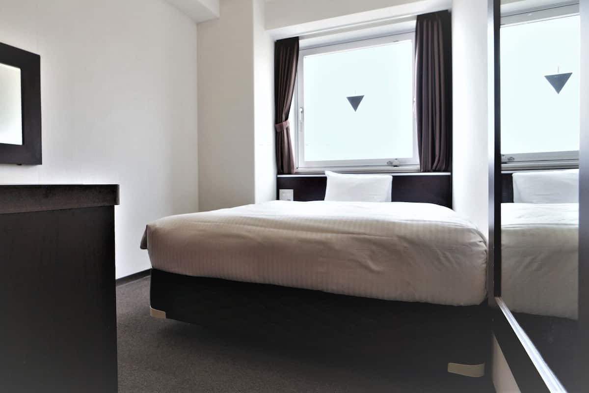 Une chambre d’hôtel avec un lit, une table de chevet, une fenêtre avec des rideaux et un miroir fixé au mur.