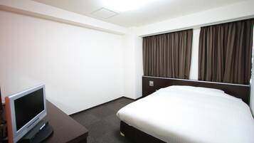 A hotel room with a bed, a TV on a desk, and curtains on the window.