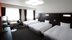 Quarto de hotel com três camas de solteiro, uma escrivaninha com um laptop, uma televisão e uma pequena mesa redonda.