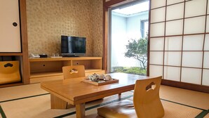 Um quarto tradicional japonês, com tatame, uma mesa de madeira baixa e uma televisão em uma prateleira.