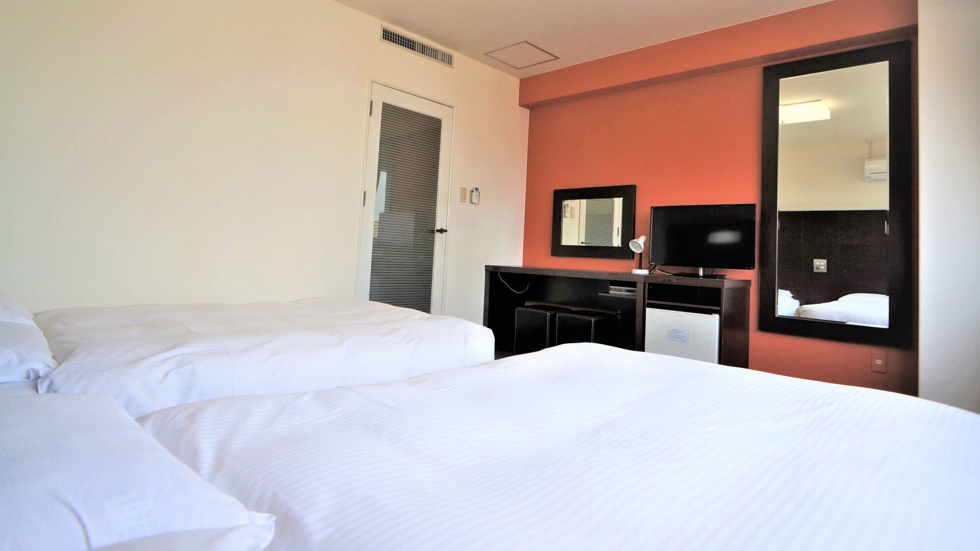 Una habitación de hotel con dos camas, un escritorio con televisor y un espejo.
