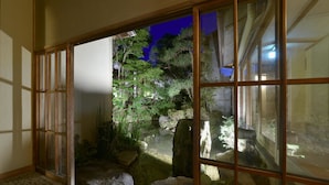 A traditional Japanese room with tatami flooring, a shoji screen door, and a view of a garden with rocks and plants.