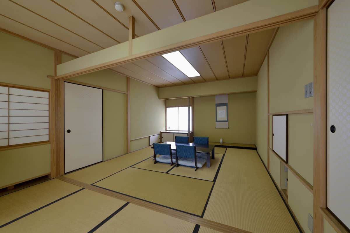 Una habitación japonesa tradicional con suelo de tatami, una mesa baja con cojines y puertas correderas.