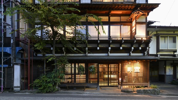 A traditional Japanese building with a wooden facade, a balcony, and a well-lit entrance.