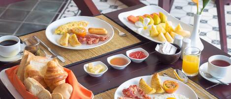 A breakfast table with croissants, eggs, ham, and fruit.
