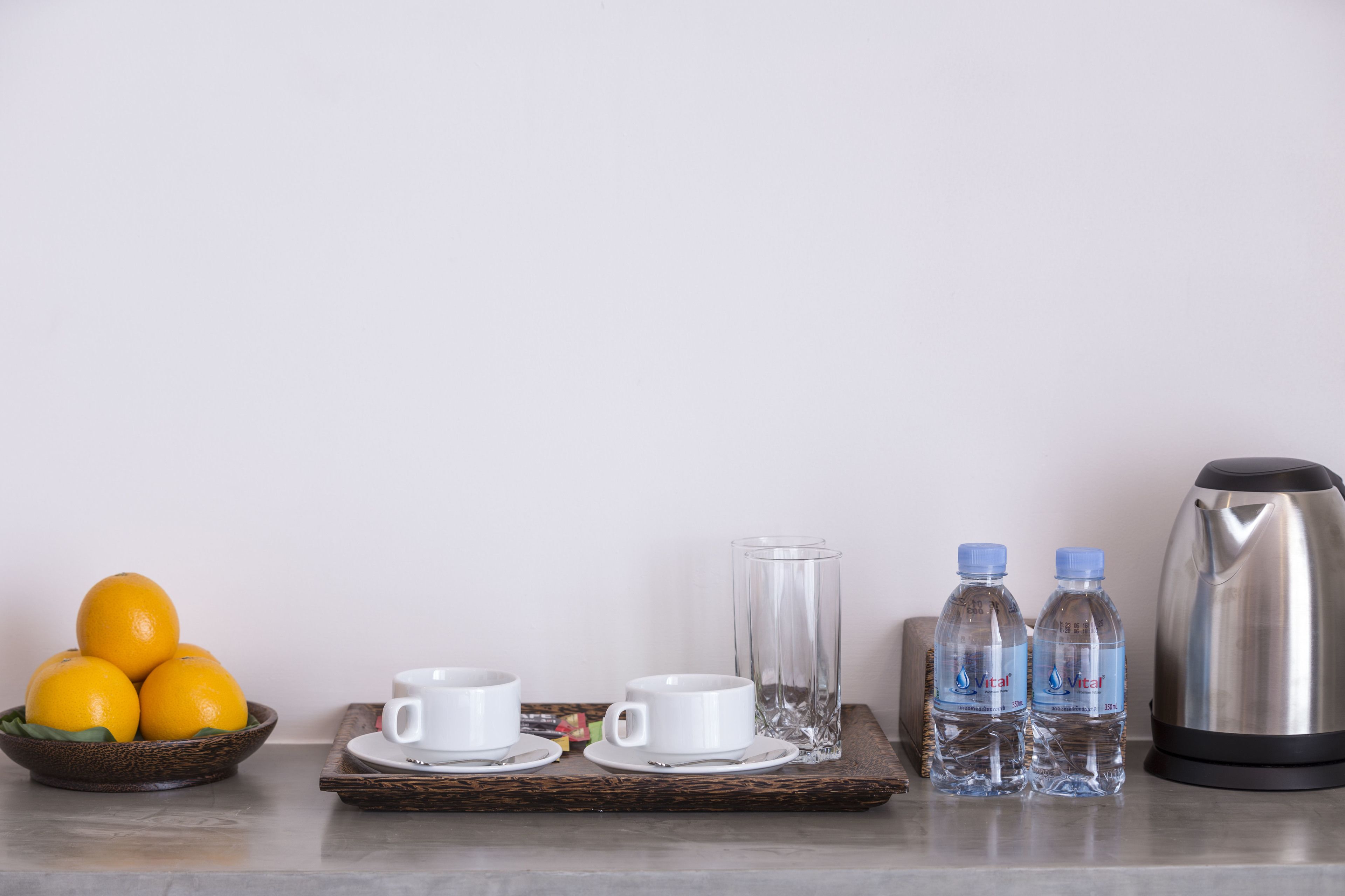 A breakfast setup with oranges, white cups, a glass, two water bottles, and a coffee pot on a tray.