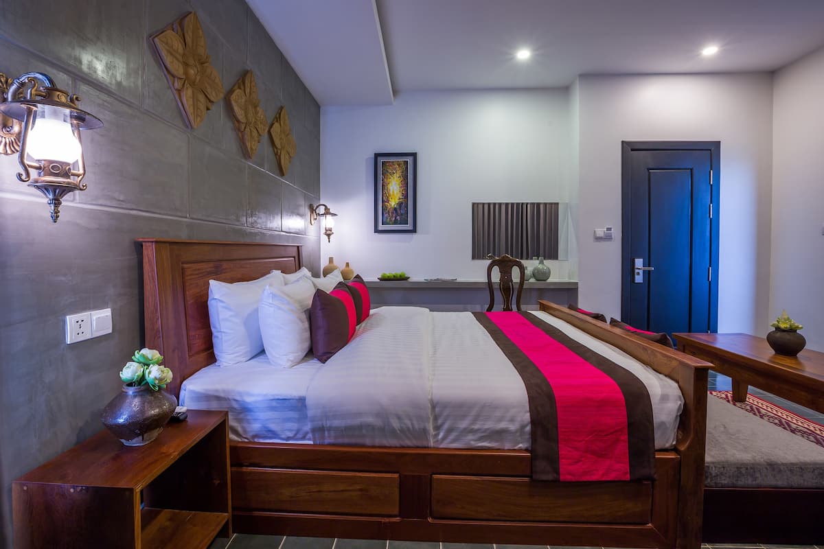 A modern hotel room with a large bed, wooden headboard, and a nightstand with a vase of flowers.