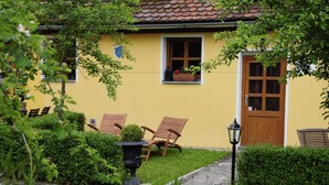 A yellow building with a tiled roof, a wooden door, and a window with a flower box. There are two wooden chairs outside and a potted plant nearby. - Hotel Schlossresidenz Heitzenhofen (Duggendorf)