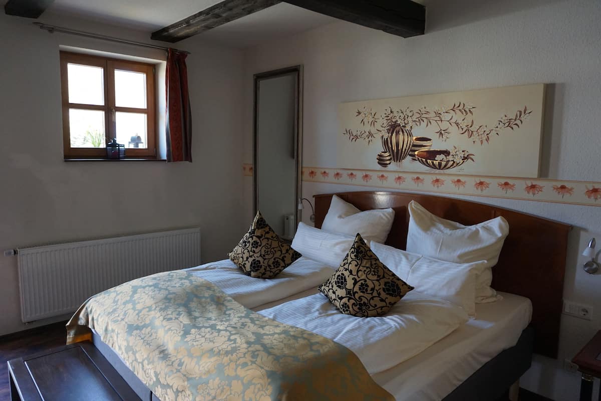 Ein Hotelzimmer mit einem Bett, einem Vorhangfenster, einem Heizkörper, einem Holzkopfstück und einem an der Wand befestigten Kunstwerk.