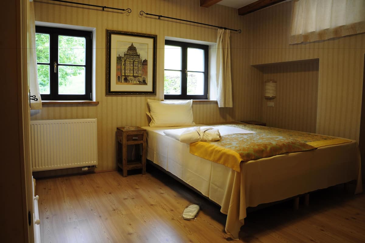 Ein Schlafzimmer mit einem Bett, zwei Fenstern, einer Heizung und einem gerahmten Bild an der Wand.