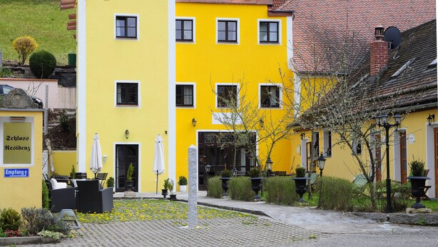 A yellow hotel building with multiple windows, outdoor seating, and a paved courtyard. - Hotel Schlossresidenz Heitzenhofen (Duggendorf)
