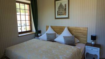 A neatly arranged hotel room with a large bed, a bedside table, a nightstand, a window with curtains, and a framed picture on the wall.